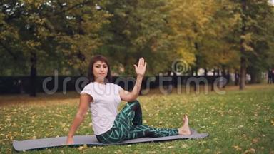 穿着运动服的漂亮女孩正在<strong>公园里</strong>锻炼身体，在温暖的秋天练习<strong>坐在</strong>瑜伽垫上的弯曲姿势